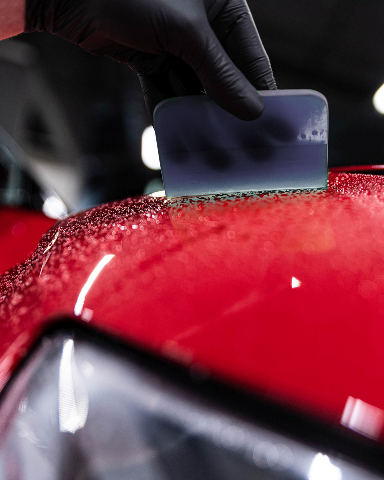 Employee of a car wash or car detailing studio applies a ceramic coating to the paintwork of a red car
